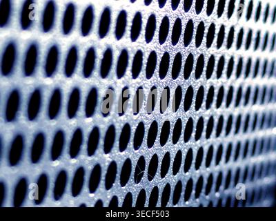 Close-up of shiny perforated metal surface with blurred background and patterned holes Stock Photo