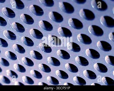 Close-up of shiny perforated metal surface with blurred background and patterned holes Stock Photo
