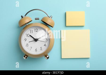 Reminder. Alarm clock and sticky notes on light blue background, flat lay Stock Photo