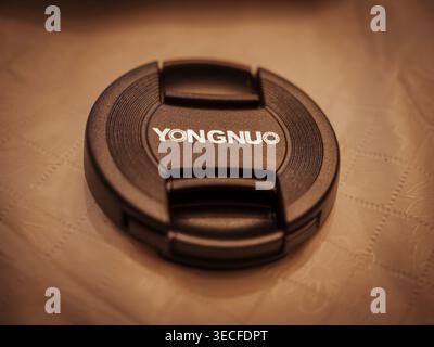 YONGNUO branded black plastic center pinch camera lens cap with white text logo sitting on a textured surface in soft warm light Stock Photo