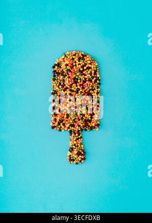 Colorful candy sprinkles shaped as ice cream popsicle on pastel blue background. Creative summer sweet candy concept. Trendy and unique flat lay. Stock Photo