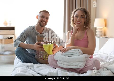 Happy couple folding fresh laundry on bed at home Stock Photo