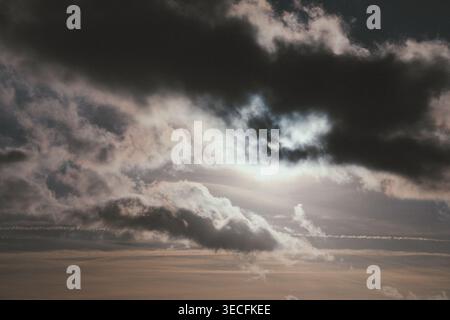 Dramatic cloudy sky with sun partially hidden behind dark storm clouds. Stock Photo