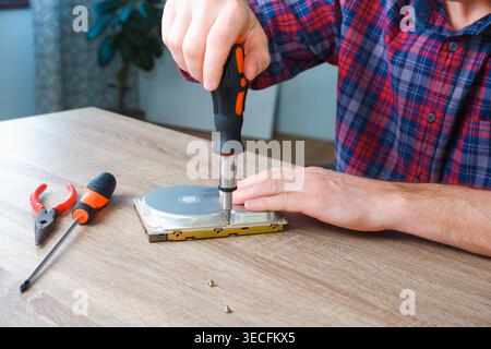 Male engineer repairman disassembles computer hard drive with a screwdriver. Concept of repairing, service, electronics and technology of computer. Stock Photo