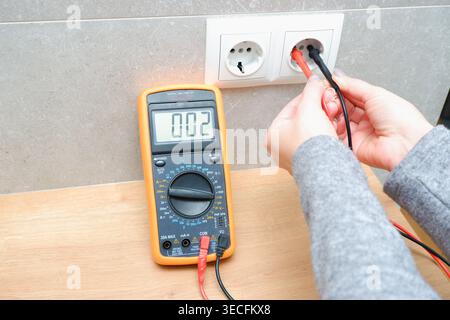 Woman with a multimeter check the voltage of the electrical network. Close-up view of the hands with the appliance near the socket. Stock Photo
