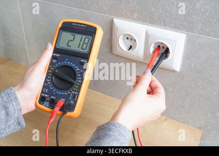 Woman with a multimeter check the voltage of the electrical network. Close-up view of the hands with the appliance near the socket. Stock Photo