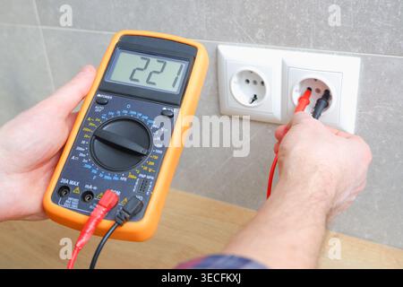 The electrician measures the voltage in the home network by inserting a voltmeter into the outlet. Measurement of voltage in electric networks Stock Photo