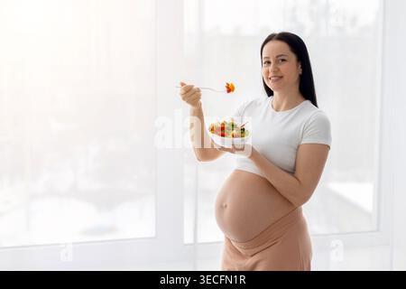 Pregnant young woman eating fresh vegetable salad, representing healthy eating habits Stock Photo