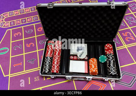 An open aluminum case filled with gambling chips, dice, and playing cards resting on a purple felt casino surface. Stock Photo