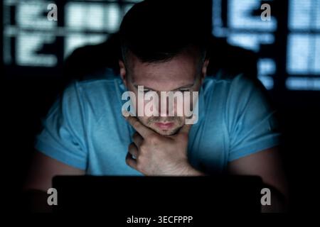 Hacker types code with concentration. Hacker analyzes network security system. Hacker monitors online data transmission. Hacker executes phishing Stock Photo