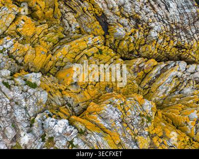 Aerial view of textured coastal rocks covered in bright yellow lichen and green moss at Silence Beach Viewpoint in Cudillero, Asturias, Spain. Stock Photo