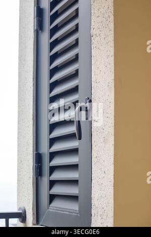 A closed gray shutter is mounted on the beige wall of the building, in the compartment containing the outdoor air conditioner unit. This is an architectural detail of the house's exterior. Stock Photo