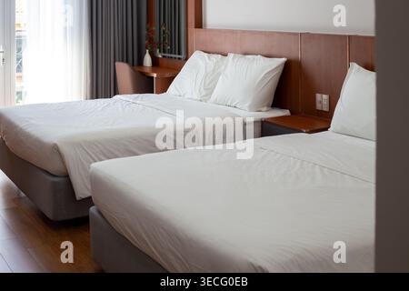 Modern hotel room interior features two twin beds made with fresh white linens. Hotel accommodation, bedroom decor, travel stay. Stock Photo