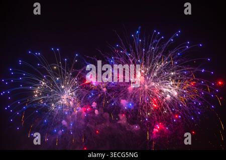 Colorful fireworks burst in the dark night sky during a festive celebration. Holiday event, night show, fireworks display. Christmas, New Year. Stock Photo