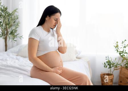 Pregnant woman holding head with hand feeling discomfort or fatigue Stock Photo