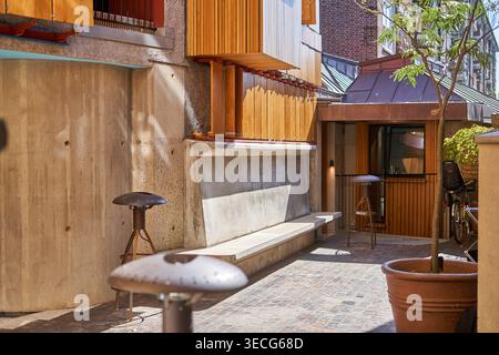 A contemporary outdoor courtyard featuring raw concrete walls with visible formwork textures, warm wooden cladding on building facades, and built-in Stock Photo