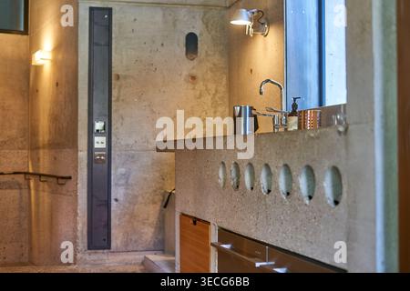 Modern industrial bathroom interior featuring exposed raw concrete walls and integrated concrete sink with decorative oval cutouts. Chrome Stock Photo
