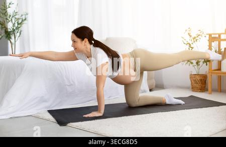 Pregnant woman on yoga mat performing bird-dog exercise on hands and knees Stock Photo