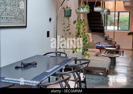 Modern open-plan residential interior featuring a dark dining table with curved black chairs and patterned placemats in the foreground, beige Stock Photo