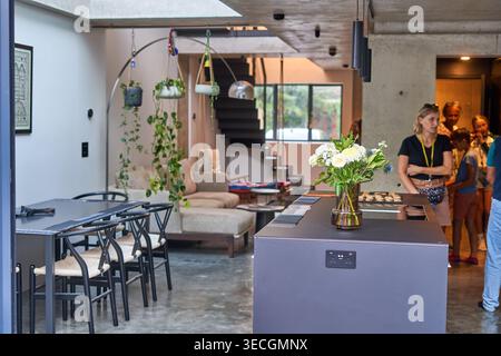 A modern open-plan interior featuring a kitchen island with a vase of white flowers in the foreground, a dining table with black chairs to the left, Stock Photo
