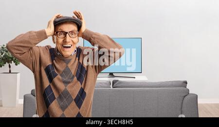 Surprised elderly man holding his head in front of a tv screen Stock Photo