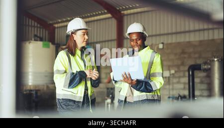 Engineer, team and talk with laptop at water plant for quality control, system efficiency or update. Manufacturing, workers and tech at wastewater Stock Photo