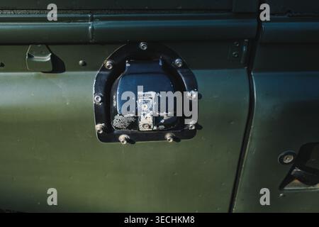 A detailed close-up shot of a black fuel filler housing and cap on the side of a classic dark green utility vehicle. Stock Photo