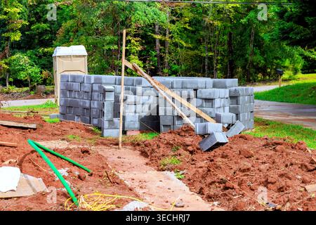 Stacks concrete blocks to form wall in forested area with tools debris around. Stock Photo
