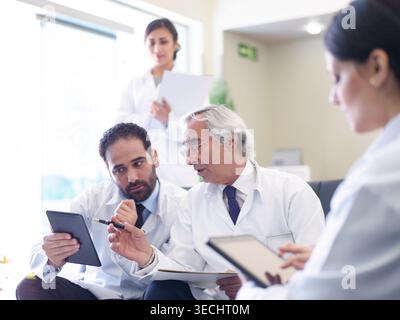 Middle Eastern doctors discussing patient care in a hospital meeting with tablets and medical notes Stock Photo