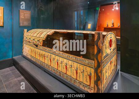 Kansas, United States, JAN 17, 2026 - An intricately painted wooden sarcophagus with colorful hieroglyphics rests on a platform inside a dimly lit mus Stock Photo