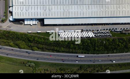 Aerial view of a large industrial warehouse with rows of white semi-truck trailers parked at loading docks next to a busy highway in Doncaster, Englan Stock Photo