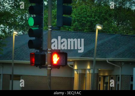 Traffic signal with illuminated red hand and green light at dusk on quiet suburban street with building and trees in background Stock Photo