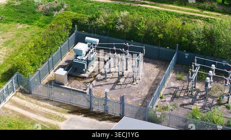 Aerial view of an electrical substation with transformers and high-voltage equipment enclosed by a security fence surrounded by lush green trees and f Stock Photo