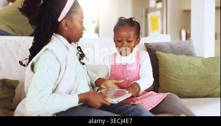 Children, home and fighting with tablet on couch, online and app disagreement with sister in lounge. Impatient, siblings and black kids with tech for Stock Photo