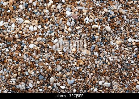Fragment of a lake shore featuring small, multicolored pebbles and gravel, suitable for use as an abstract background or texture. Stock Photo