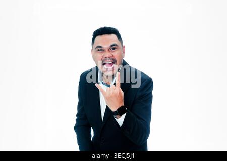An Indonesian man in a black suit shouting and showing a rock sign gesture, expressing excitement, success, and energy on a white background. Stock Photo