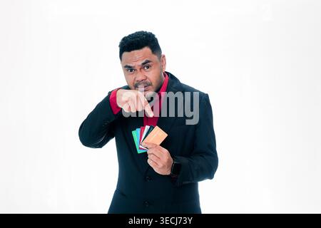 Portrait of an Indonesian man in a suit pointing his finger at a fan of credit cards with a serious expression, isolated on white background. Stock Photo