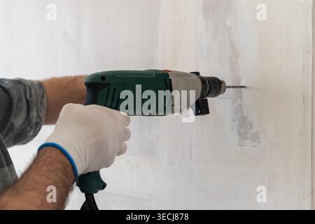 A technician operates an electric power drill, creating holes in a wall during a home renovation project. The environment is well lit with visible textures of the wall and tools nearby. Stock Photo