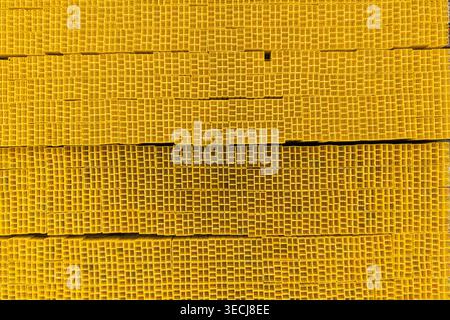 Aerial view of stacked yellow square industrial pipes arranged in a dense grid pattern with repetitive geometric textures. Stock Photo