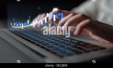 A focused close-up image shows hands typing on a laptop keyboard while digital graphs and statistics float above, representing financial data and Stock Photo