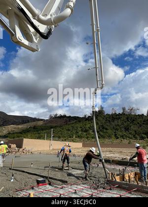 Construction workers pouring, vibrating and finishing concrete slab with hand tools at active building site Stock Photo