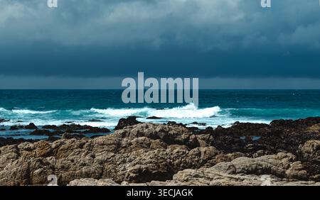 Dramatic dark storm clouds gather over the rugged rocky coastline and turquoise waves of the Pacific Ocean in California. Stock Photo