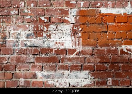 Macro horizontal full frame background texture of shabby weathered brick wall surface painted with patches of white and red paint Stock Photo