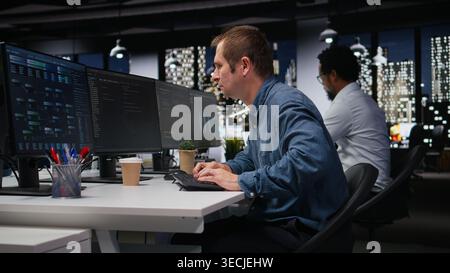 System administrator in company workplace doing artificial intelligence tech quality assurance. Man in office typing on keyboard, writing AI script with programming languages Stock Photo