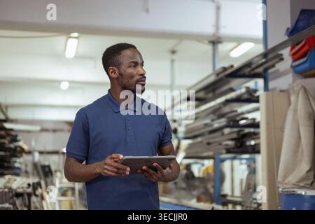 African American metal factory manager taking inventory using a tablet for modern, digital supply chain management in heavy industry. Stock Photo