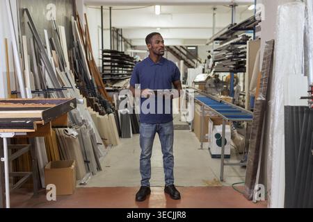 African American metal factory manager taking inventory using a tablet for modern, digital supply chain management in heavy industry. Stock Photo