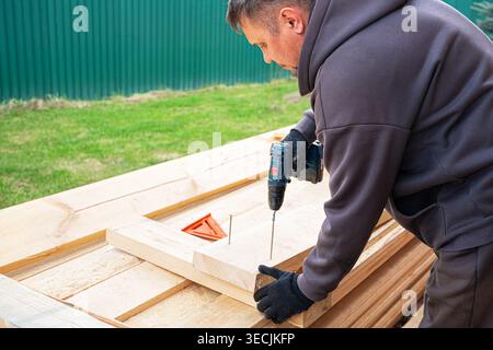 Carpenter man using electric screwdriver to fasten wooden planks, copy space. Work in progress,  frame house construction. DIY eco wooden home concept Stock Photo