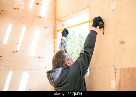 Carpenter man measuring a window frame in new house under construction. Professional unrecognizable constructor using ruler to check window on wooden Stock Photo