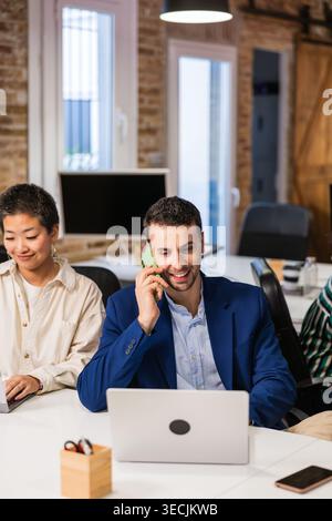 Businessman talking on phone and working on laptop in modern office Stock Photo