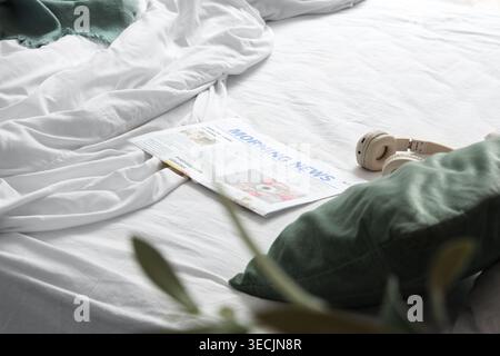 Headphones with newspaper on unmade bed in hotel room Stock Photo